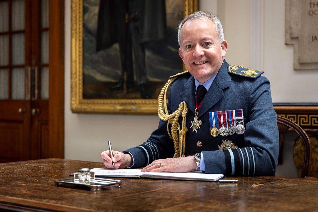 Air Chief Marshal Sir Richard Knighton seated at his desk in full naval regalia